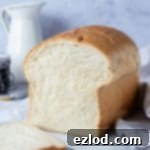 A loaf of vegan sandwich bread on a marble board with a white jug and a jar of jam.