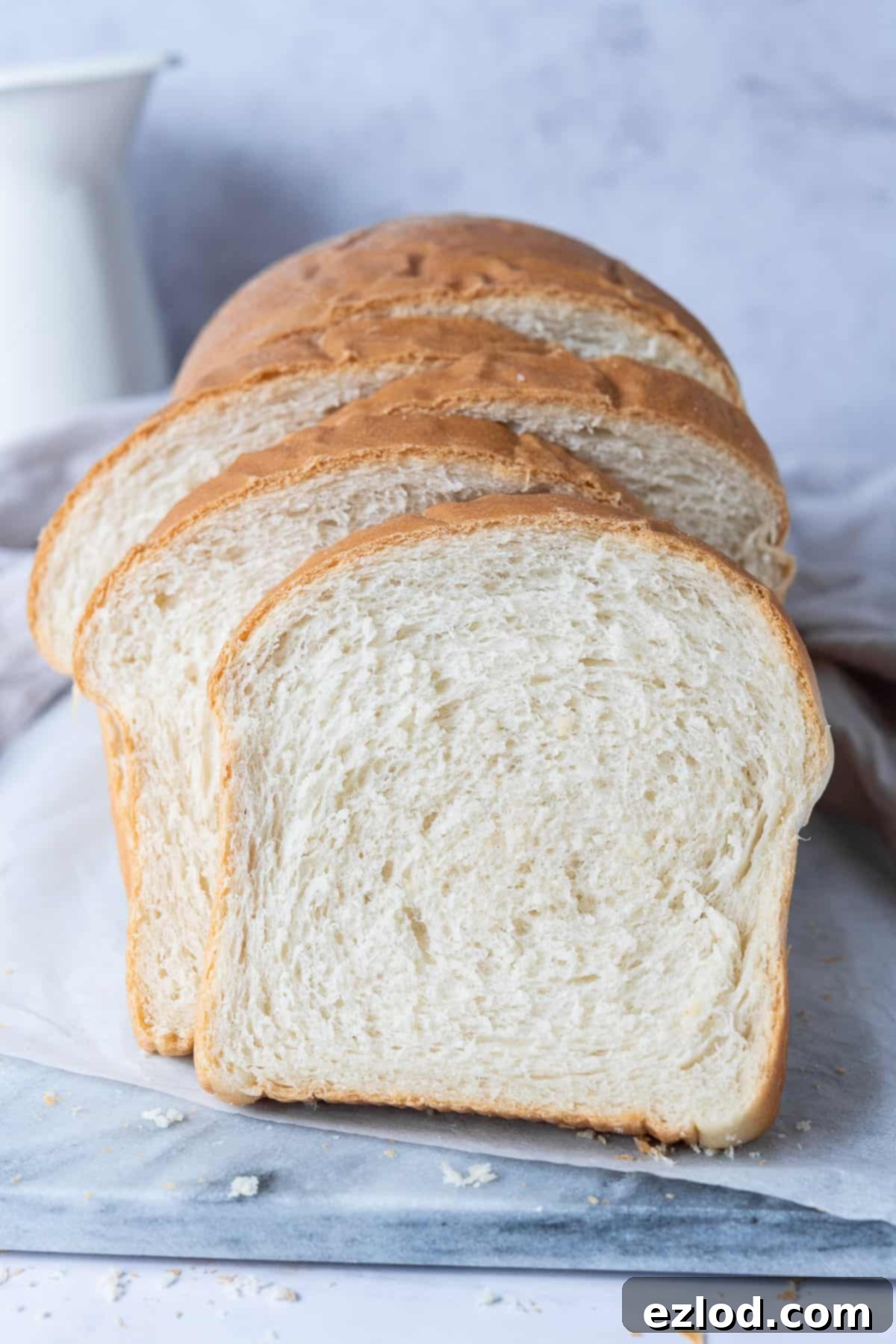Several slices of freshly baked vegan sandwich bread are arranged neatly on a marble board, highlighting the soft, airy texture of the bread.