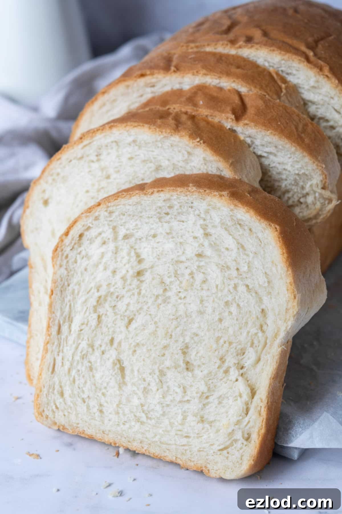 Several slices of vegan bread are artfully arranged on a marble surface, emphasizing their soft texture and golden crust, ready to be enjoyed.