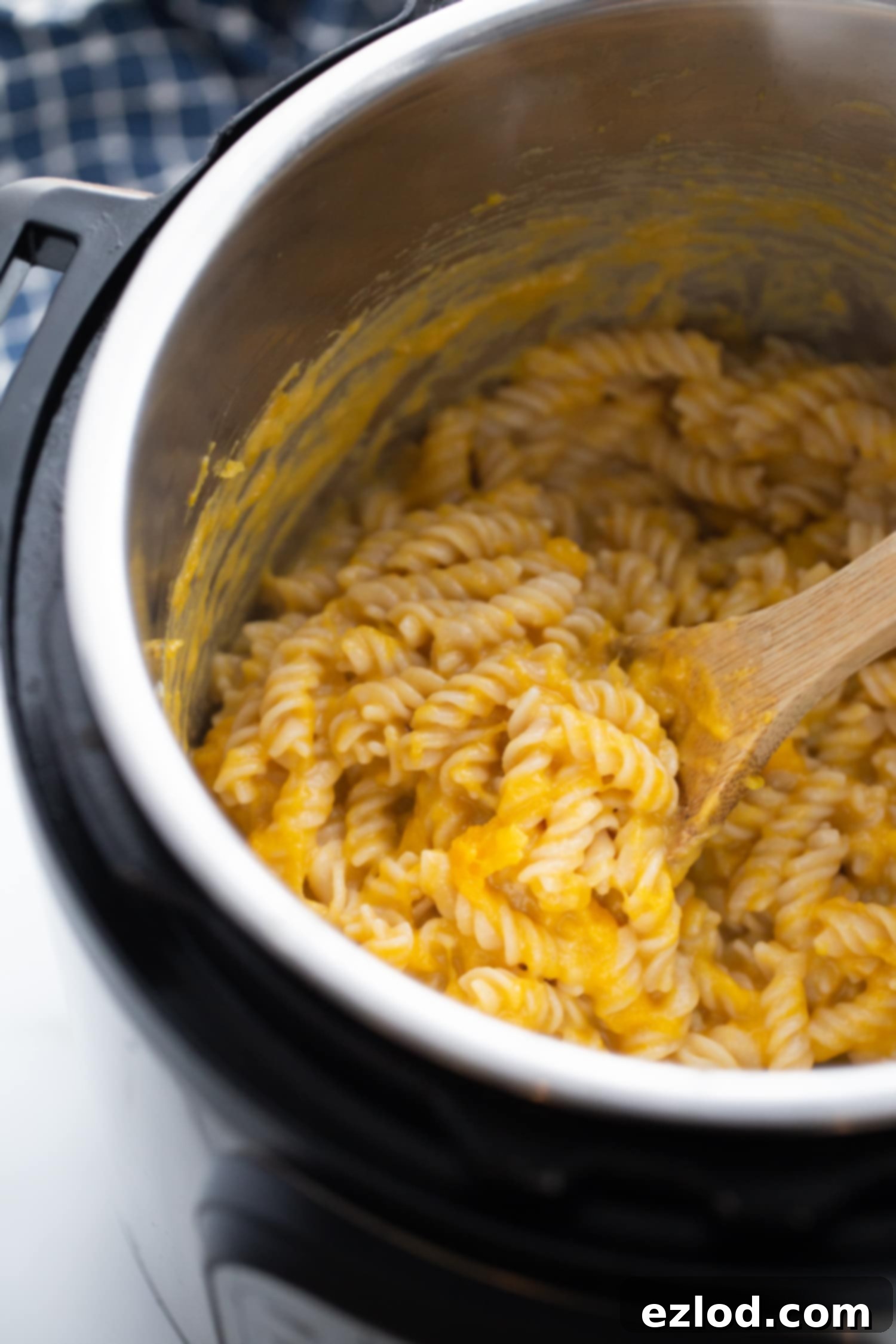 Cooked pasta in the instant pot being mixed by a wooden spoon.