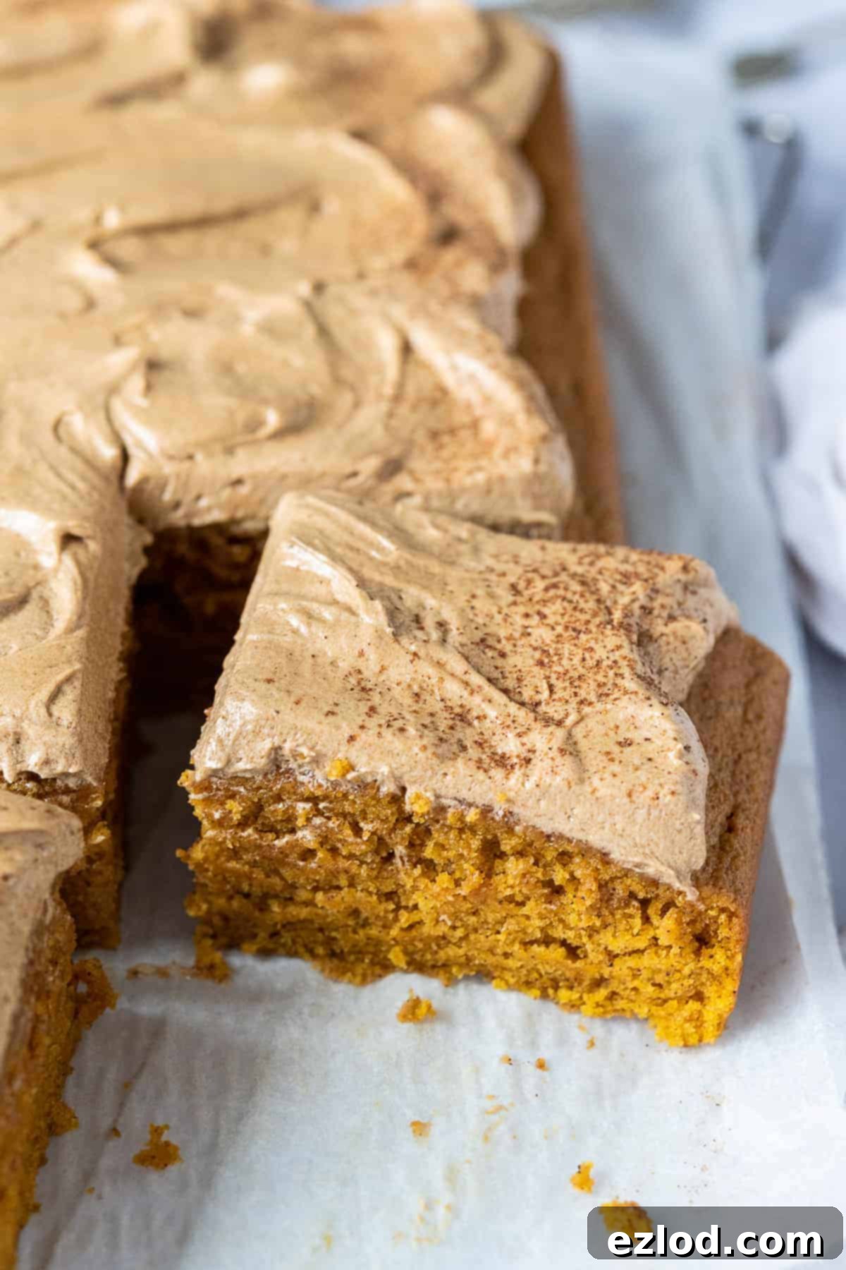 A close-up shot of a perfect slice of vegan pumpkin spice latte cake, showcasing its moist, golden-orange cake base and the creamy, swirled coffee buttercream topping.