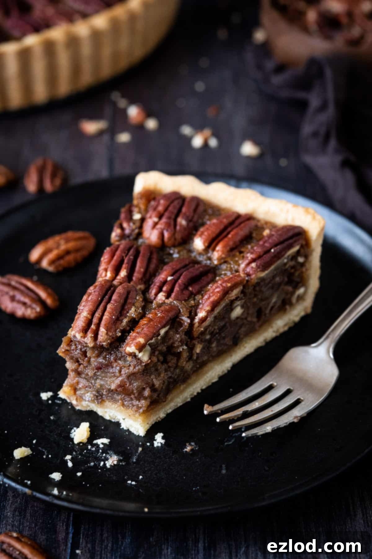 Close up of a slice of vegan pecan pie on a black plate with a forkful removed.