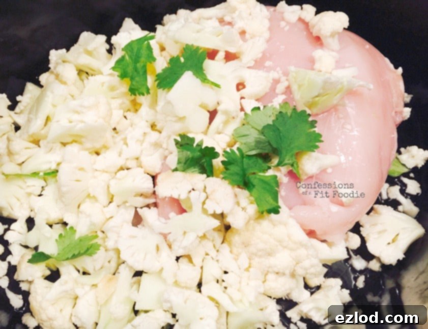 Cauliflower, raw chicken, and cilantro in a crock pot, ready to be cooked into a delicious, healthy chili.