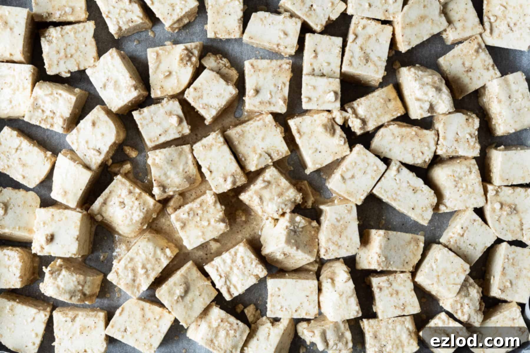 Close-up view of cubed tofu 'paneer' pieces, perfectly coated in a savoury marinade and arranged on a baking sheet, ready for the oven to transform them into golden, flavourful bites for Vegan Palak Paneer.