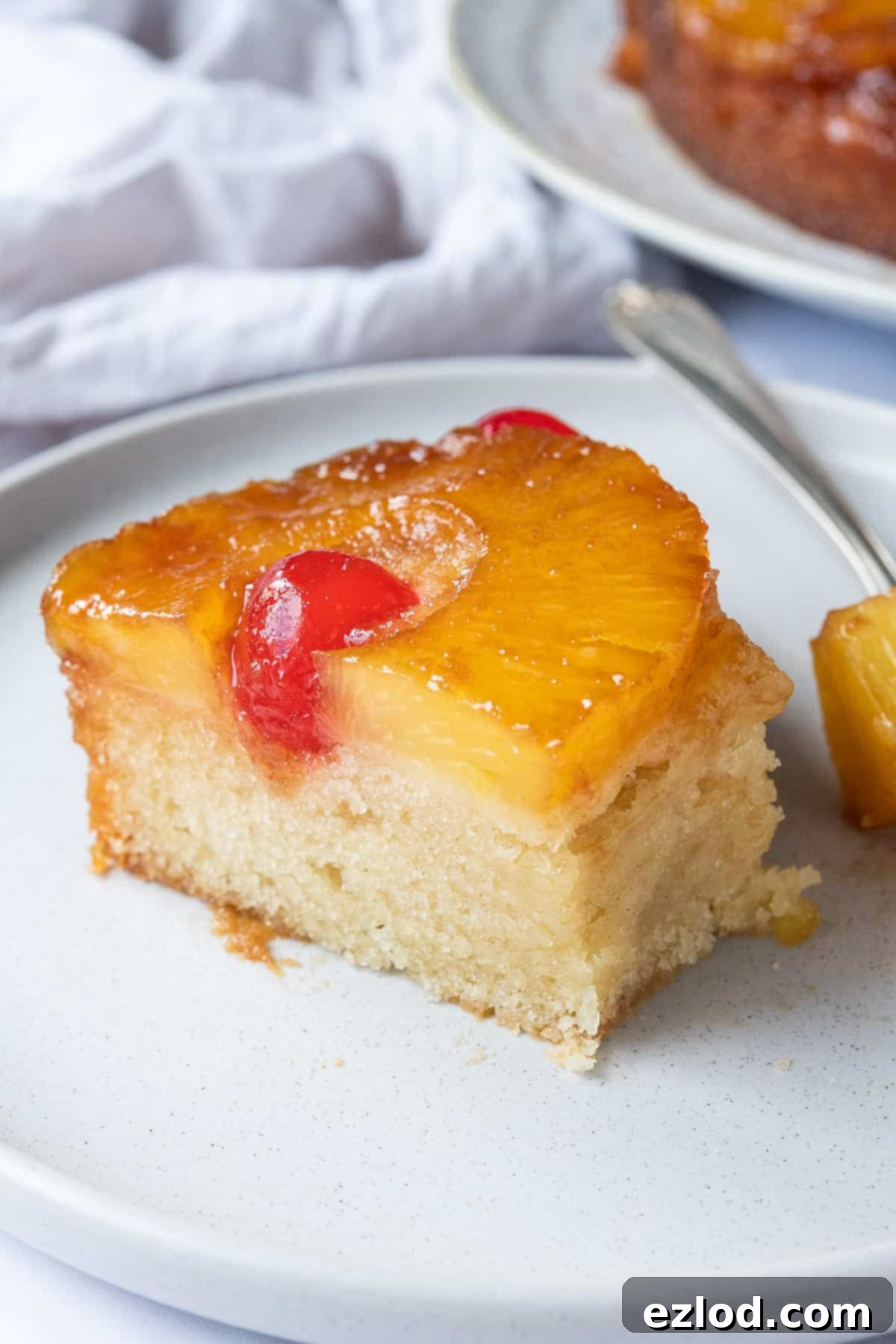 A delectable slice of vegan pineapple upside-down cake on a plate, with a fork removing a perfect bite, highlighting the moist texture and fruity topping.