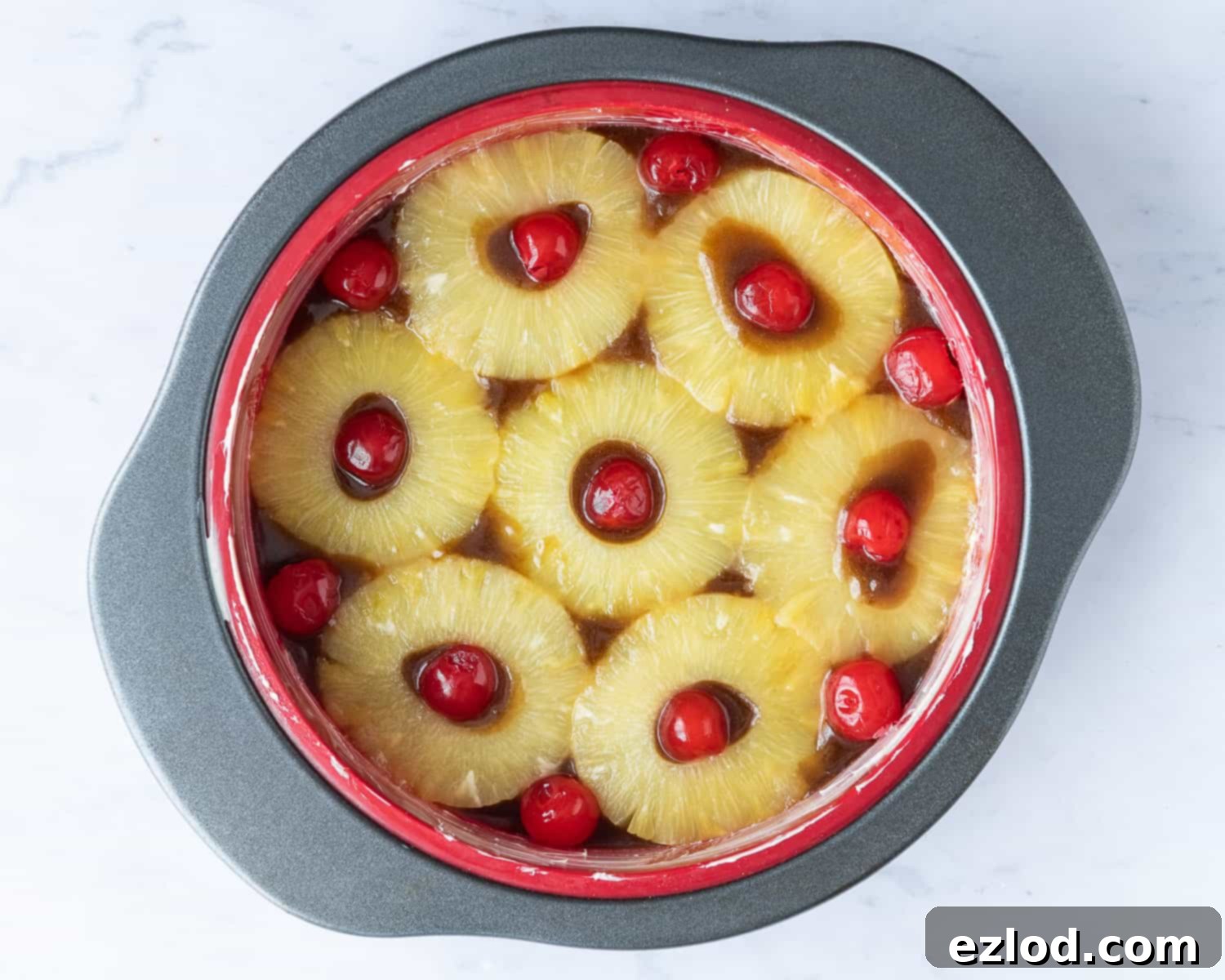 Step-by-step image showing the arrangement of pineapple rings and cherries at the base of a cake tin, preparing for the vegan upside-down cake.