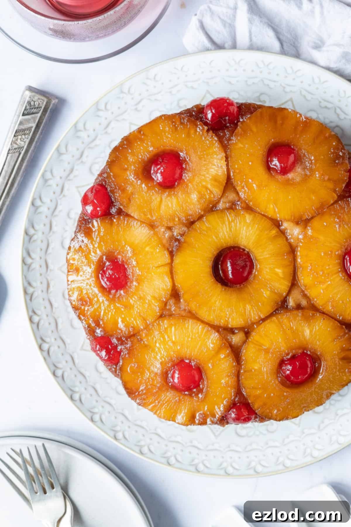 A close-up of a beautifully inverted vegan pineapple upside-down cake on a white plate, showcasing the perfectly caramelized pineapple and juicy cherries.