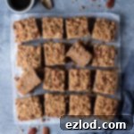 Vegan banana crumb cake sliced into squares on a grey background with a cup of espresso, a grey cloth and chopped pecans.