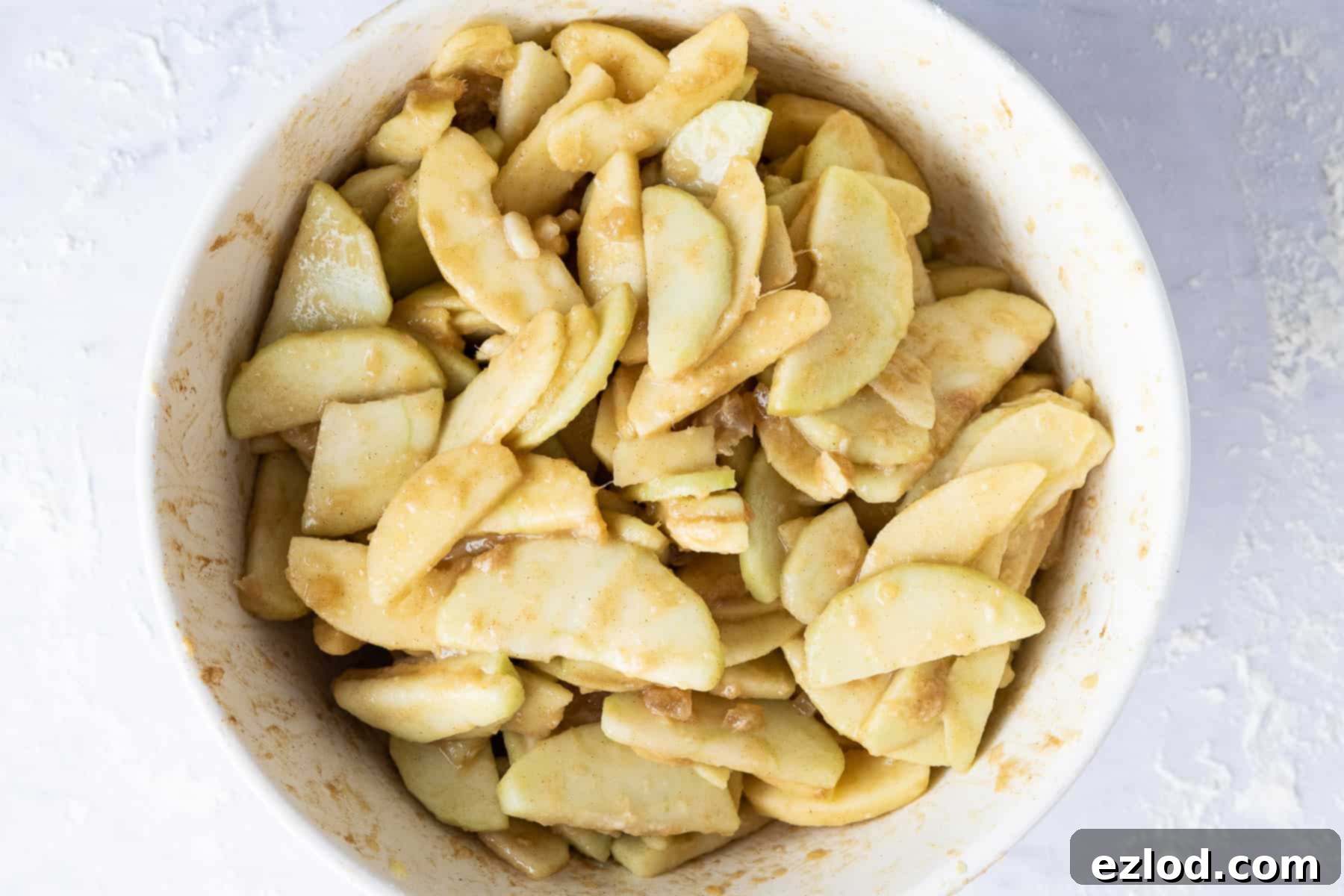 Step-by-step image illustrating the preparation of the vegan ginger apple pie filling, showing sliced apples mixed with spices, sugar, and ginger in a large bowl.