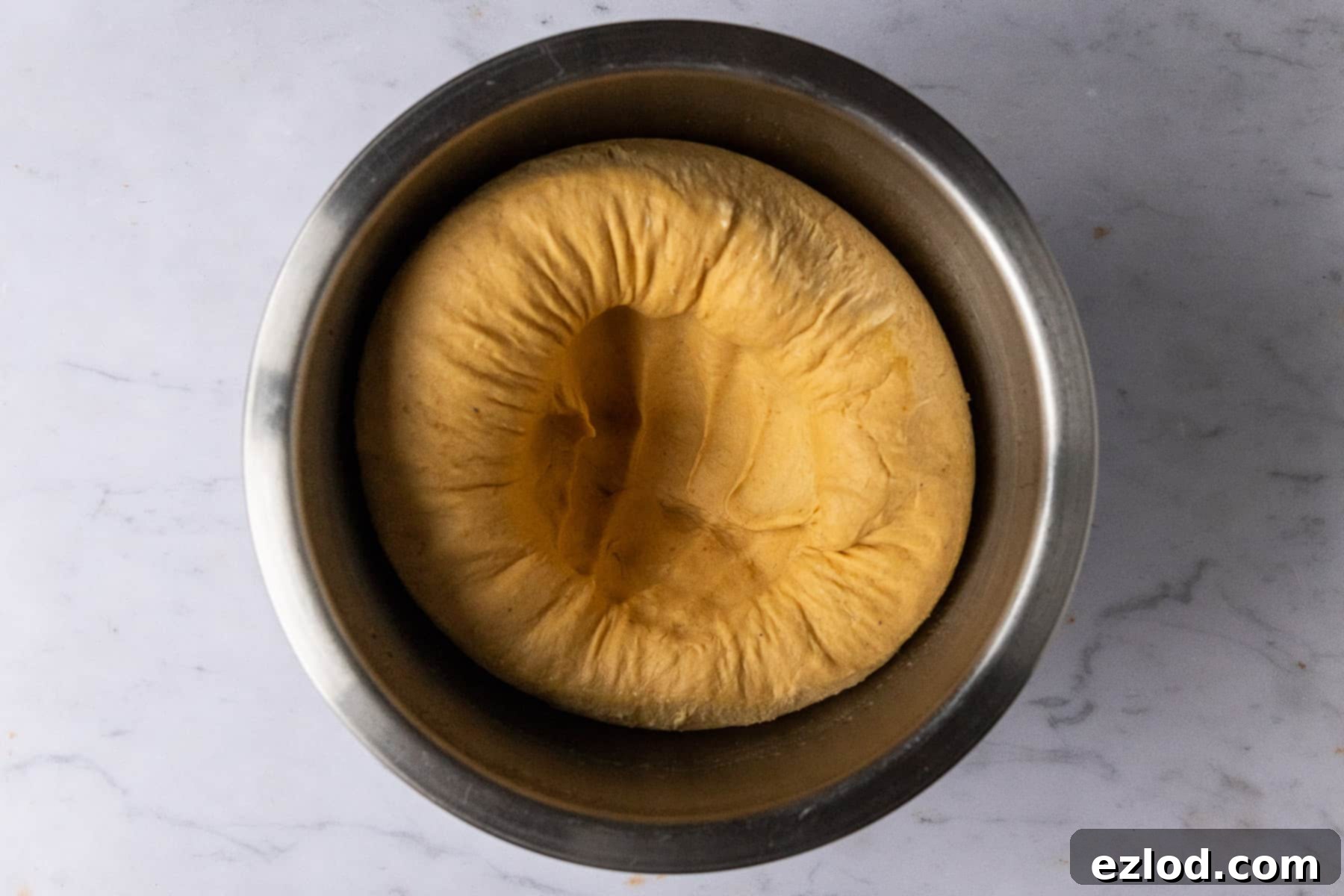 Step 4 in making vegan pumpkin cinnamon rolls: a hand gently punching down a risen dough in a bowl, showing how the air is released.