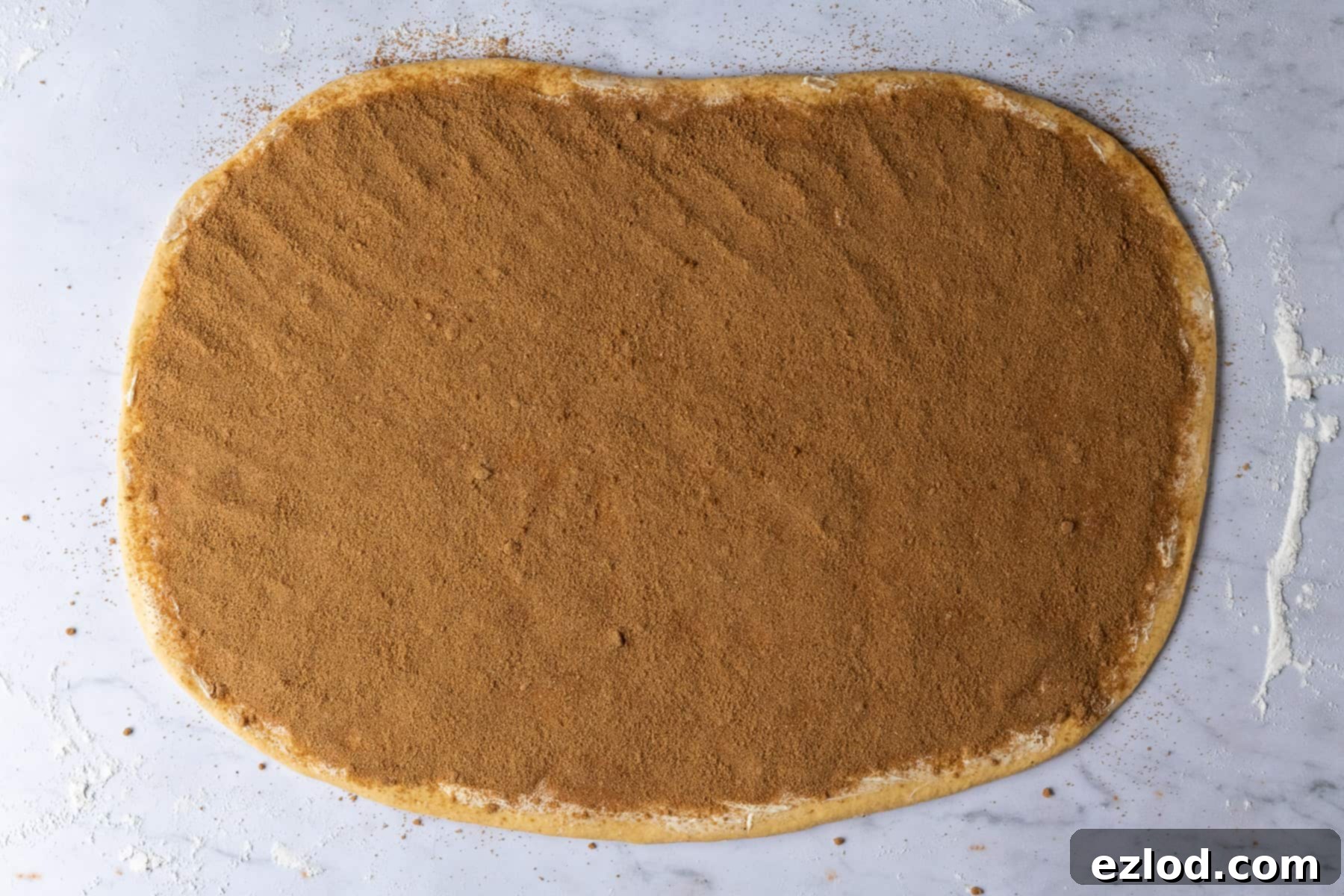 Step 5 in making vegan pumpkin cinnamon rolls: dough rolled out into a rectangle, with softened vegan butter and spiced brown sugar filling evenly spread, ready to be rolled.