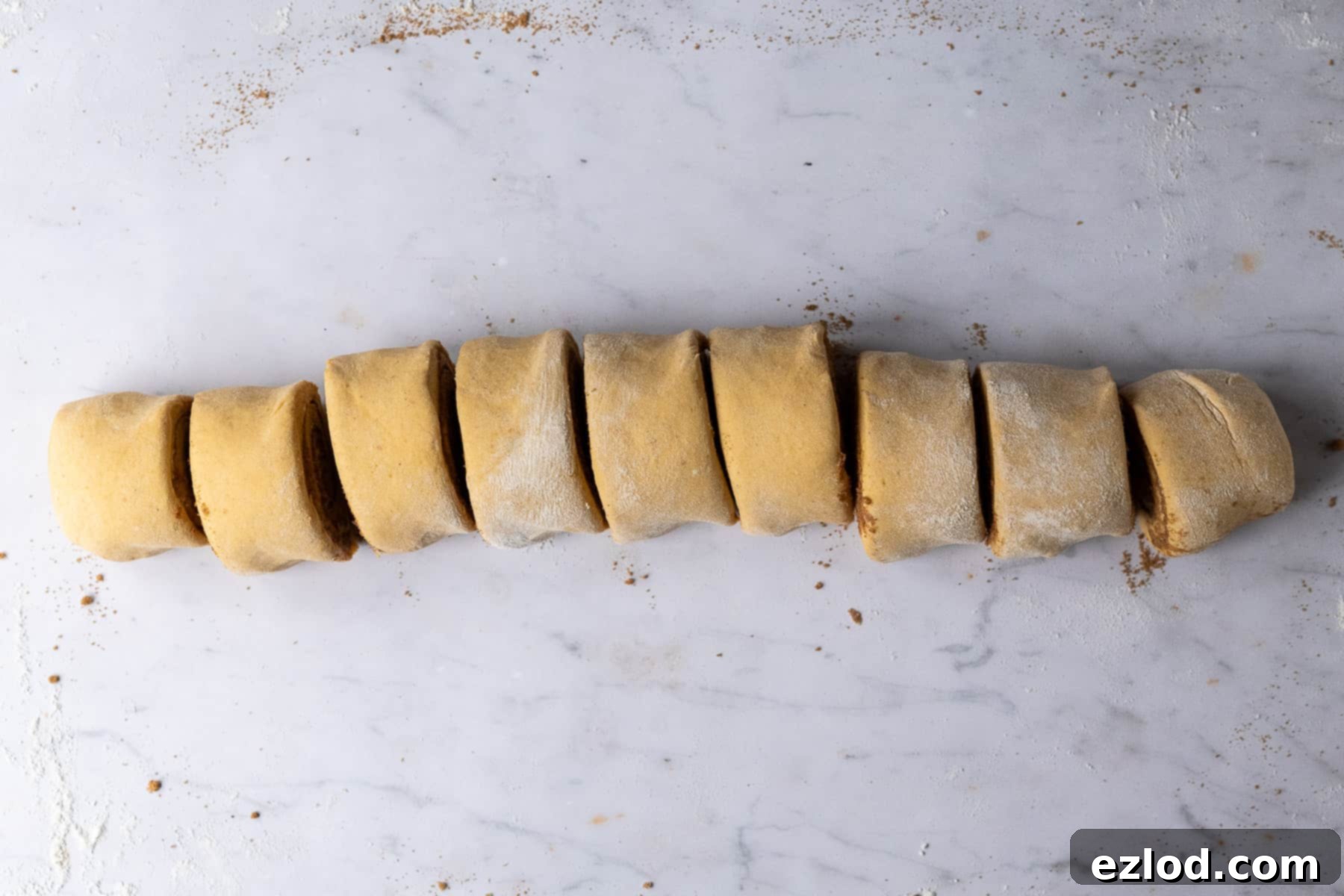 Step 6 in making vegan pumpkin cinnamon rolls: the dough is rolled up tightly into a log, then precisely sliced into individual rolls ready for baking.