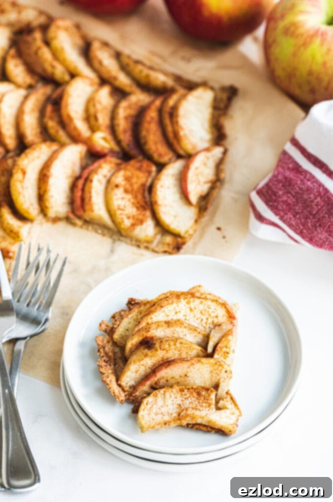 A perfectly portioned piece of gluten-free apple tart resting on a pristine stack of white plates, accompanied by two elegant forks, with the rest of the tempting apple tart visible in the background, creating a mouth-watering scene.