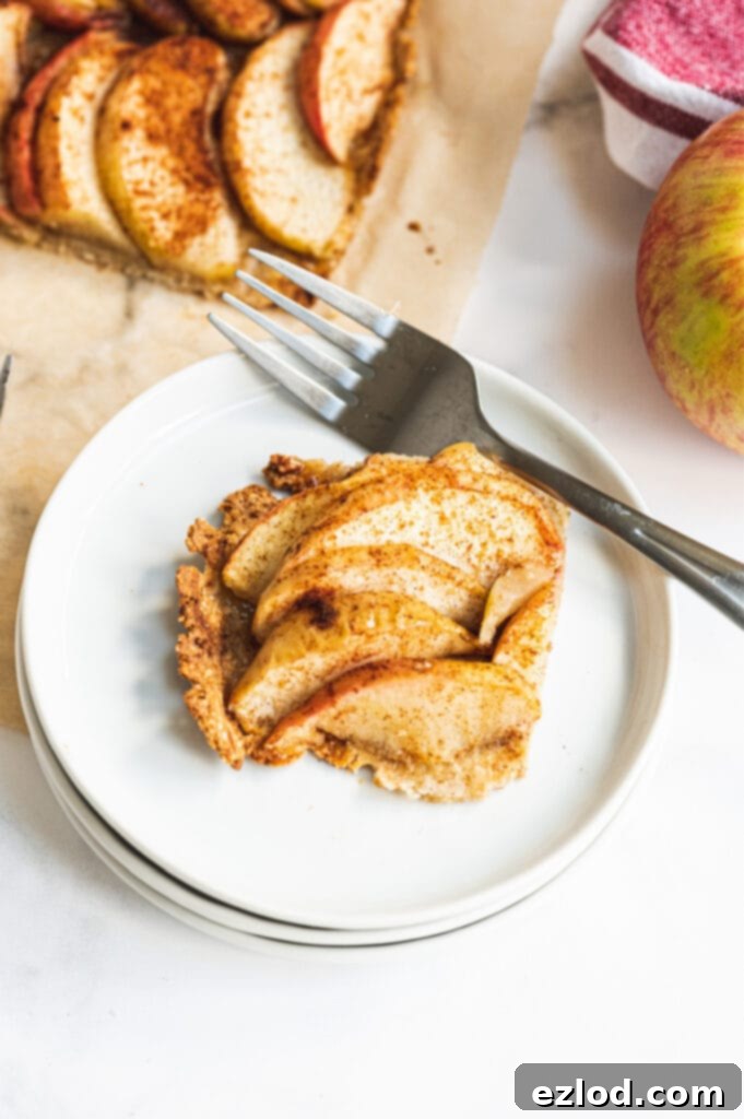 A charming piece of gluten-free apple tart beautifully presented on a pristine white plate, with a fork gently resting on the side, inviting a delicious first bite.