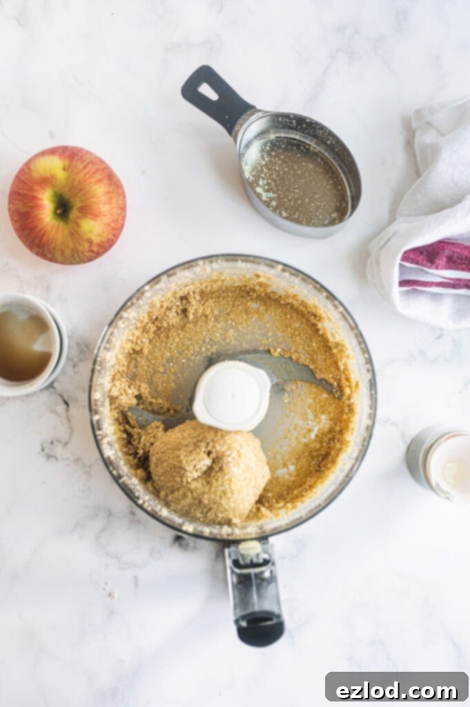 An overhead shot showcasing a food processor containing a perfectly formed ball of Gluten-Free dough, primarily crafted from a blend of almond flour and oat flour, ready for the next step in the tart-making process.