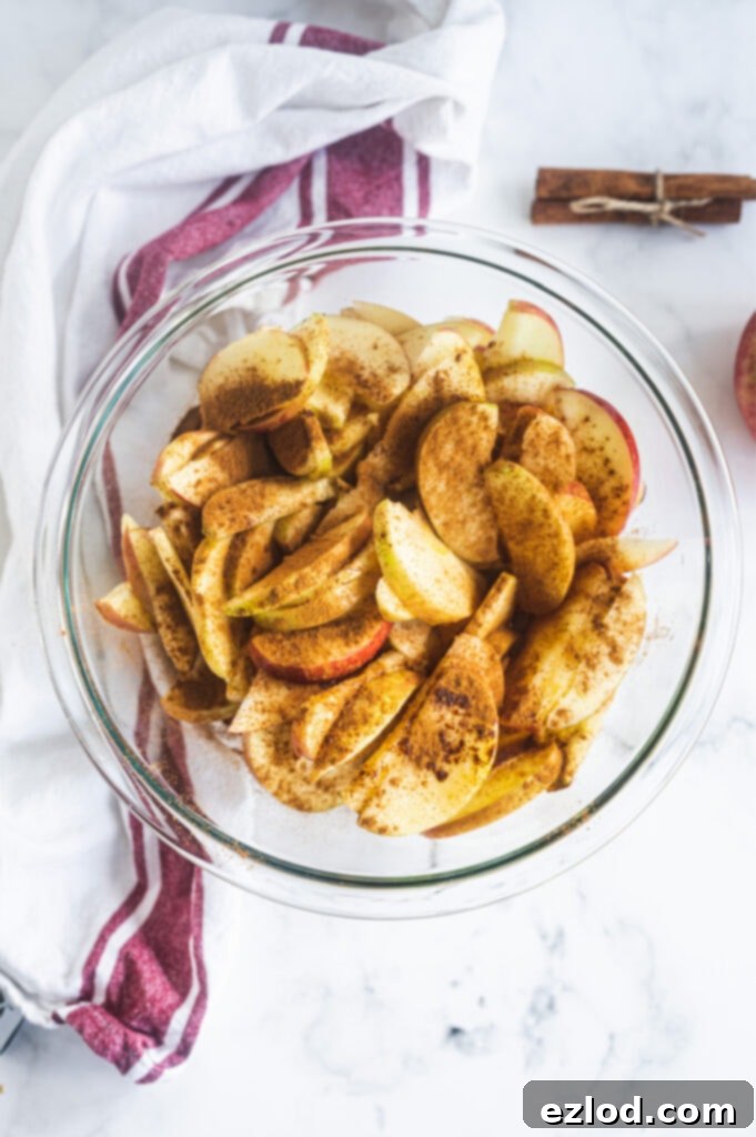 A vibrant glass bowl filled with perfectly sliced apples, generously coated with cinnamon, ready to become the delicious topping for the tart.