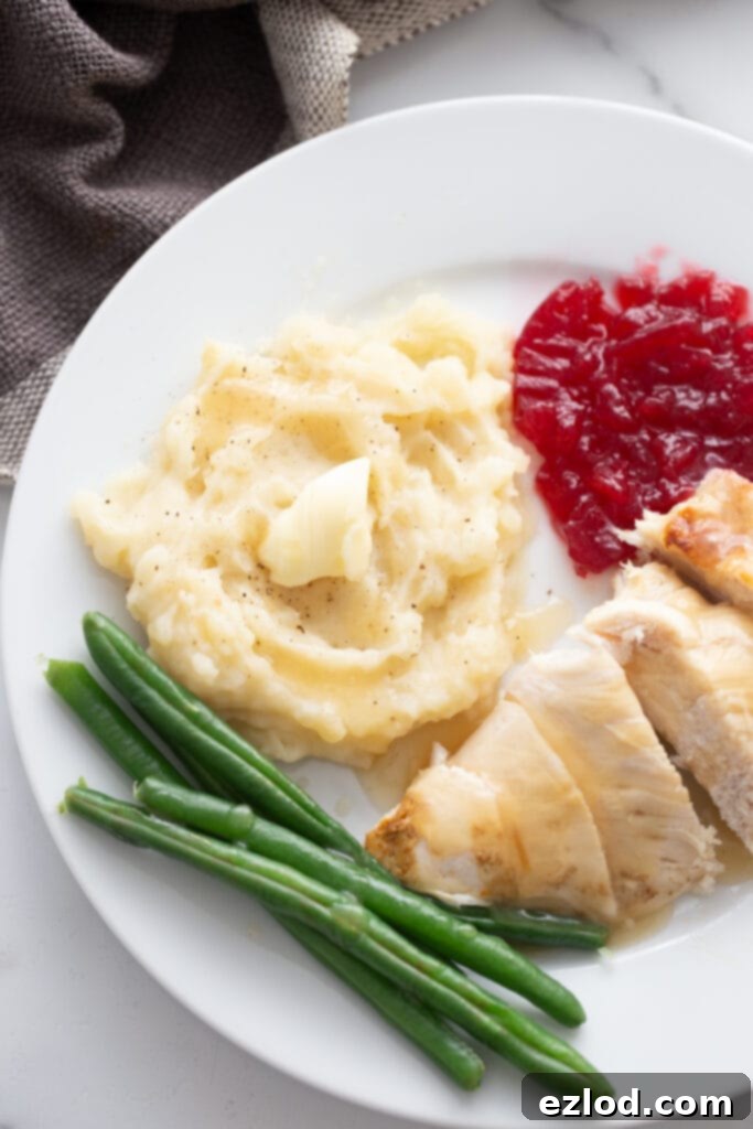 Sliced turkey breast with gravy, mashed potatoes with butter, green beans, and cranberry sauce on a white plate.