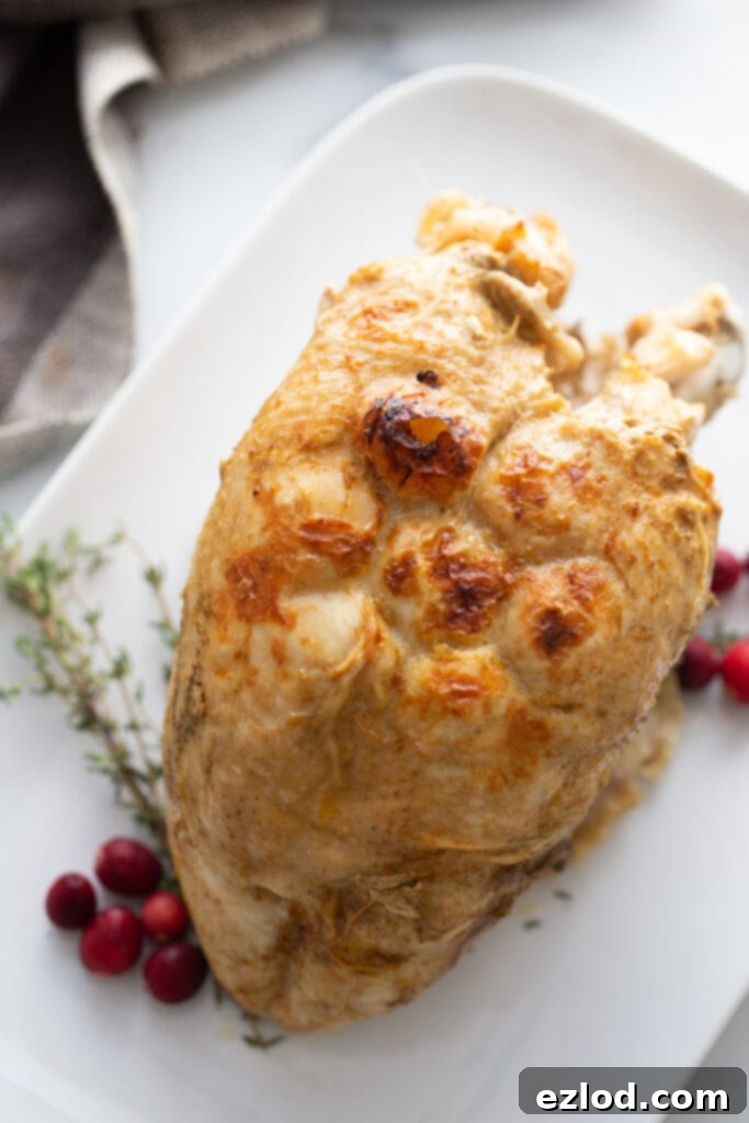 Instant pot turkey breast with crispy skin on a white serving dish. Cranberries and thyme are garnishes on the side.