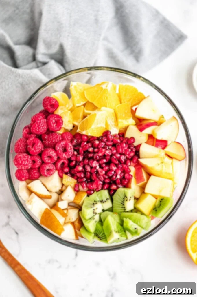 Several diced fruits are placed in a glass bowl on a white marble surface.