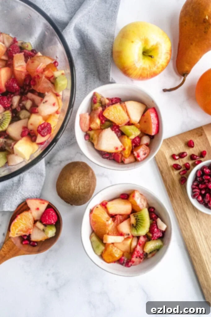 Two servings of fruit salad are placed in small white bowls, next to a wooden serving spoon.