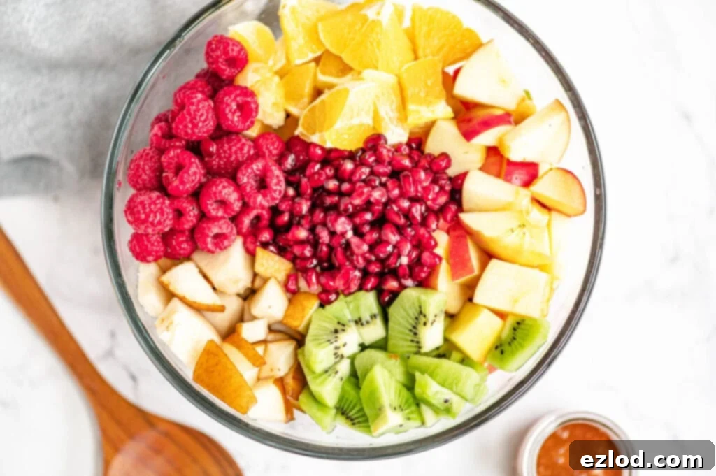 Multiple diced fruits are placed perfectly in a large glass bowl on a white marble surface.