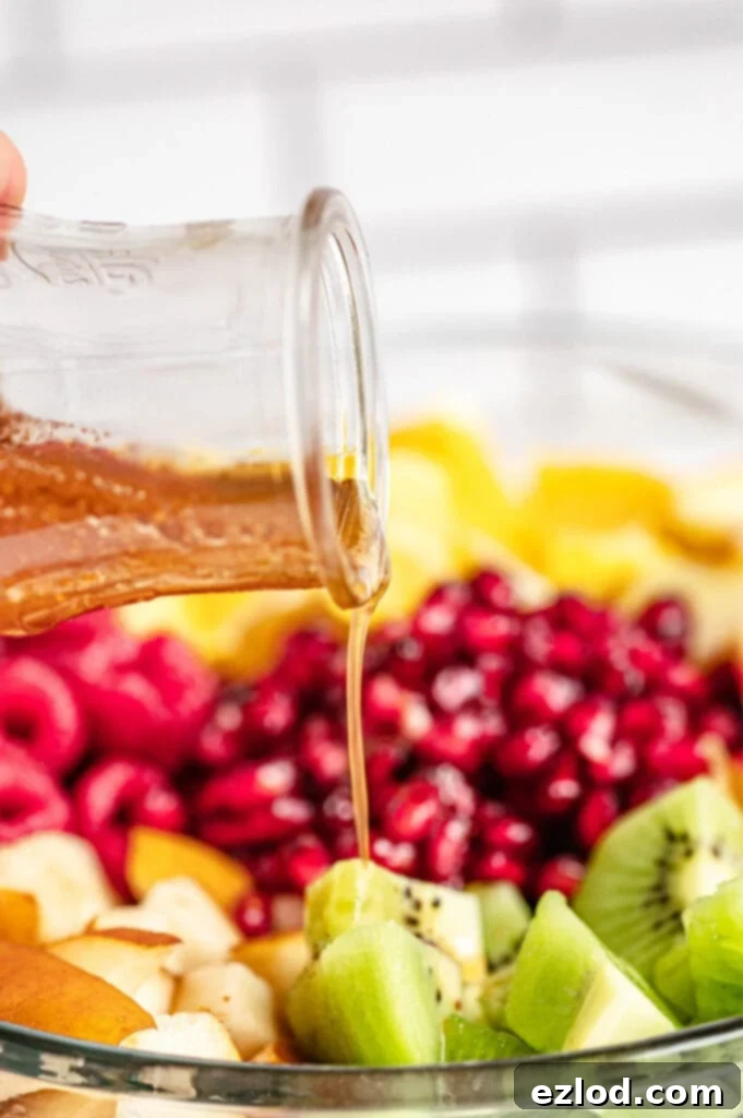 Maple syrup in a glass container is drizzled over pieces of green kiwi.