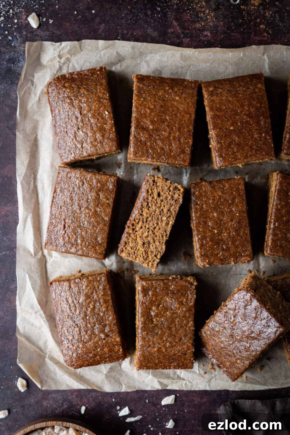 Vegan parkin cut into individual bars and arranged on a piece of rustic brown baking parchment, showcasing its sticky texture and golden-brown crust.