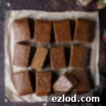 Vegan parkin on a dark brown surface with jars of spices, a tin of treacle and a bowl of crystallised ginger.