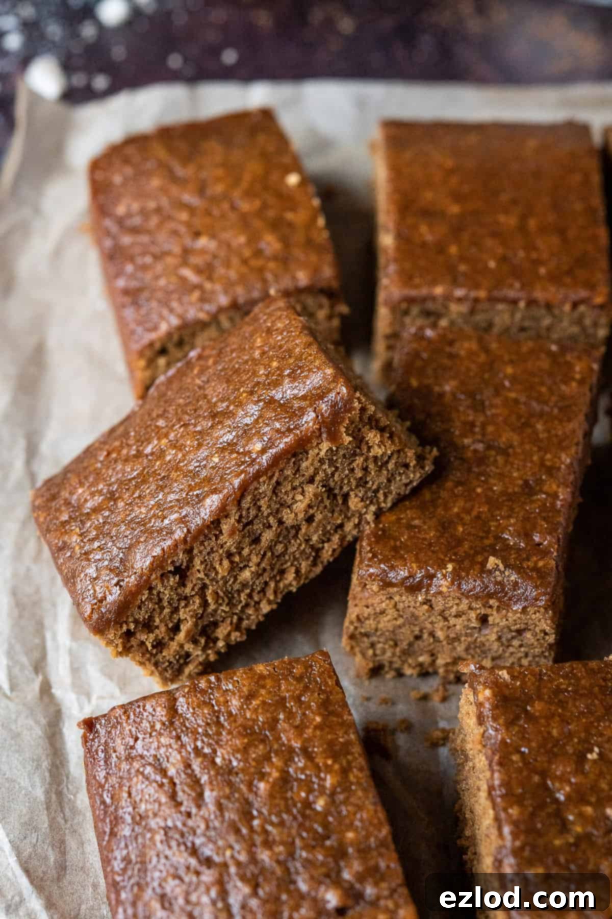A perfectly square slice of vegan parkin with a sticky, dark brown interior, resting on a dark surface, highlighting its moist and dense texture.