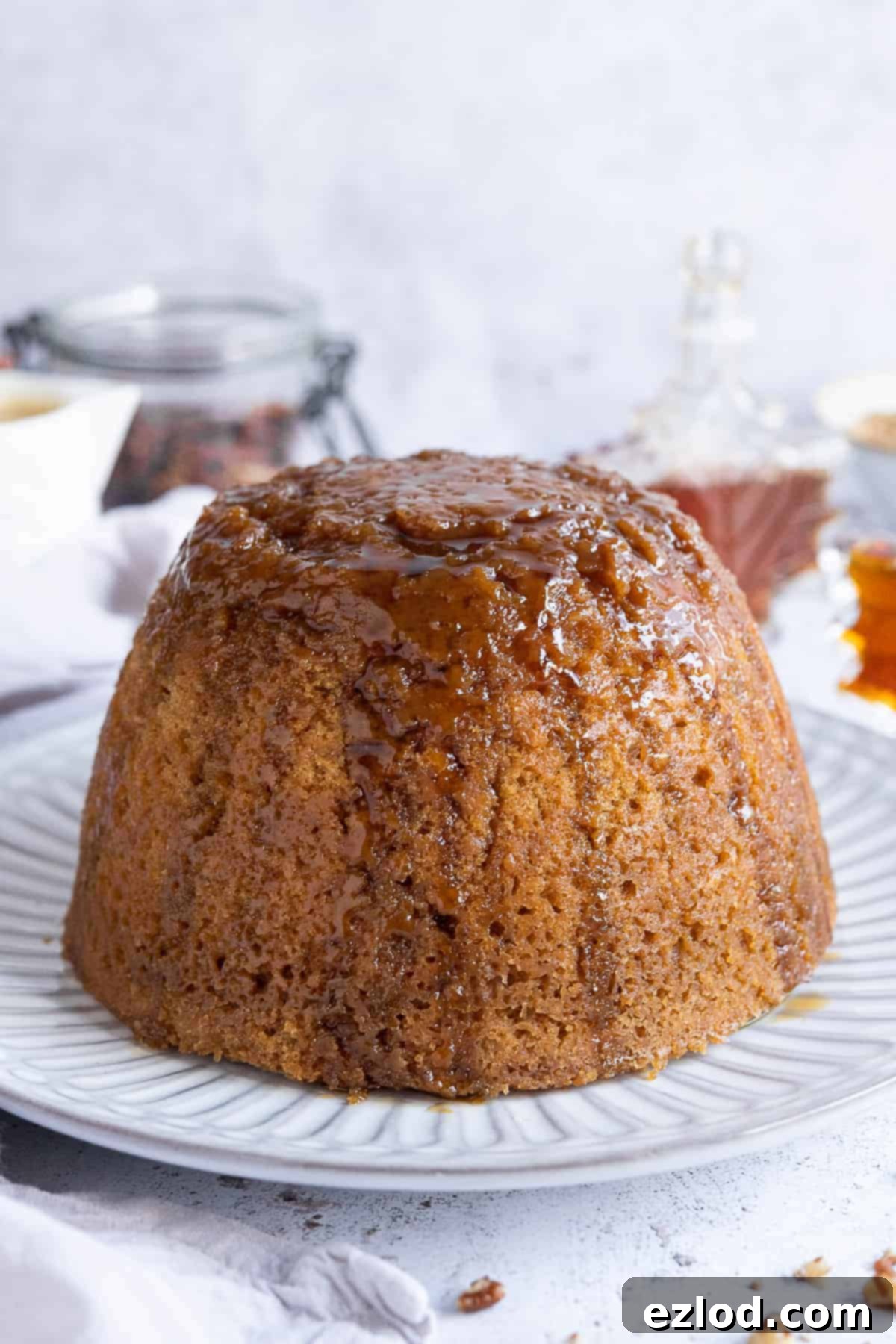 Close up of vegan steamed maple syrup pudding on a white plate, showcasing its golden, moist texture.