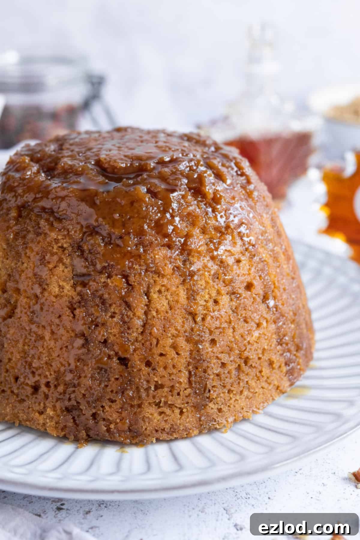 Close up of vegan steamed maple syrup pudding topped with a generous drizzle of maple syrup, ready to be served.