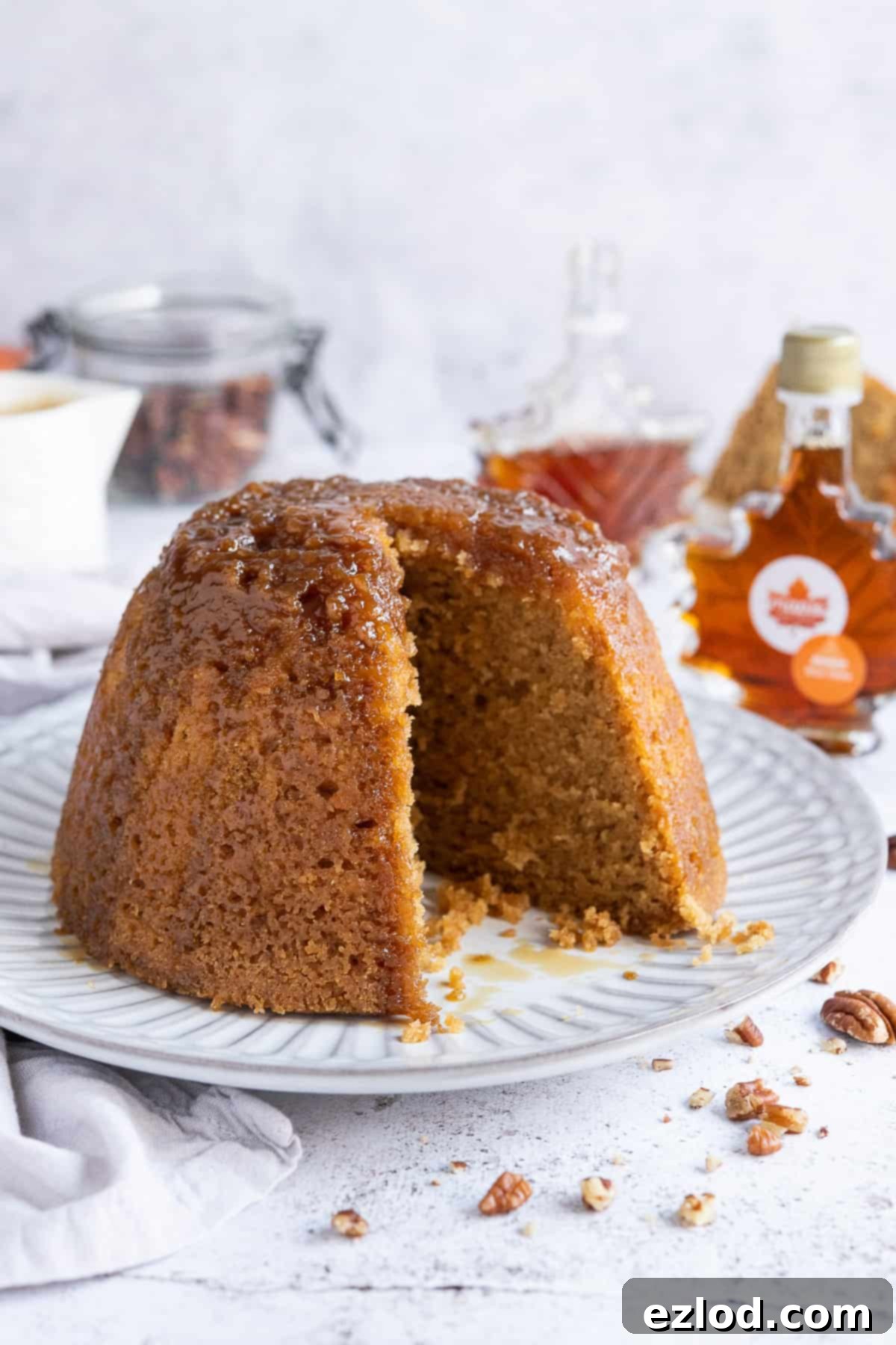 Steamed maple syrup pudding on a white plate with a slice removed, revealing its moist interior.