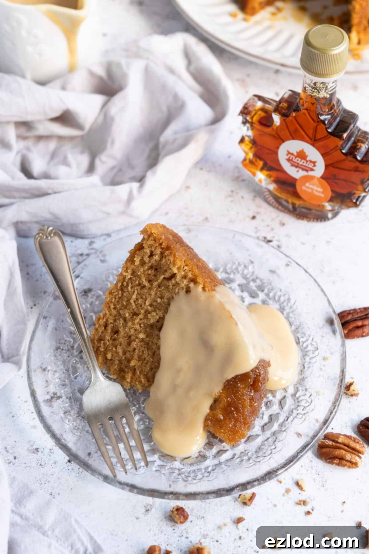 A slice of vegan steamed maple syrup pudding topped with generous maple custard on a glass plate with a fork, ready to be enjoyed.