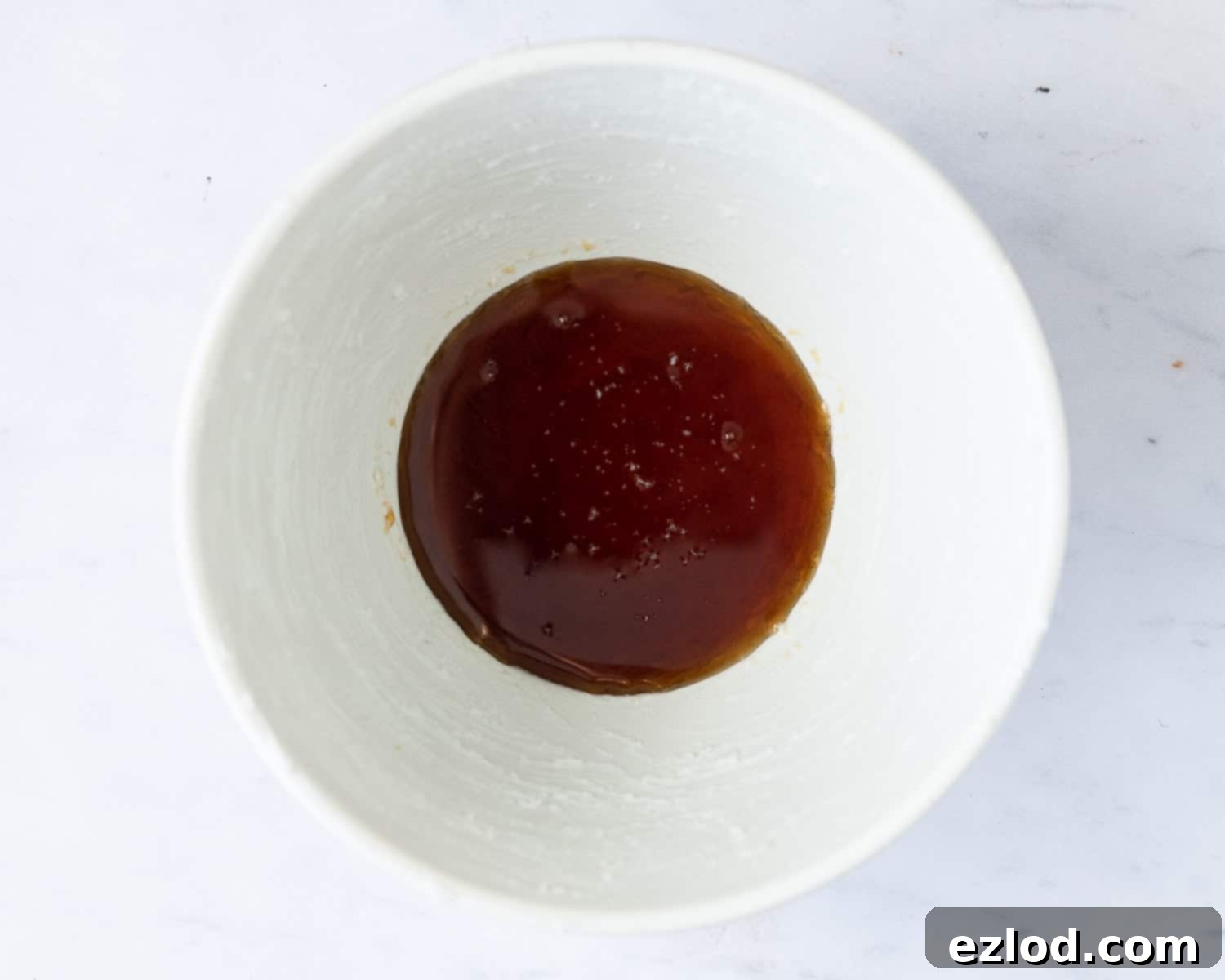 Step 1 in making vegan steamed maple syrup pudding: thoroughly greasing the pudding basin and adding maple syrup.