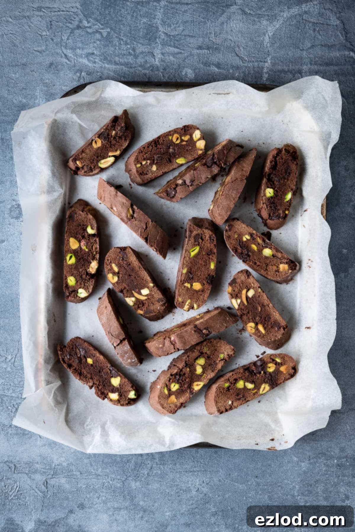 Chocolate pistachio biscotti displayed on a baking parchment-lined baking tray against a soft grey background.