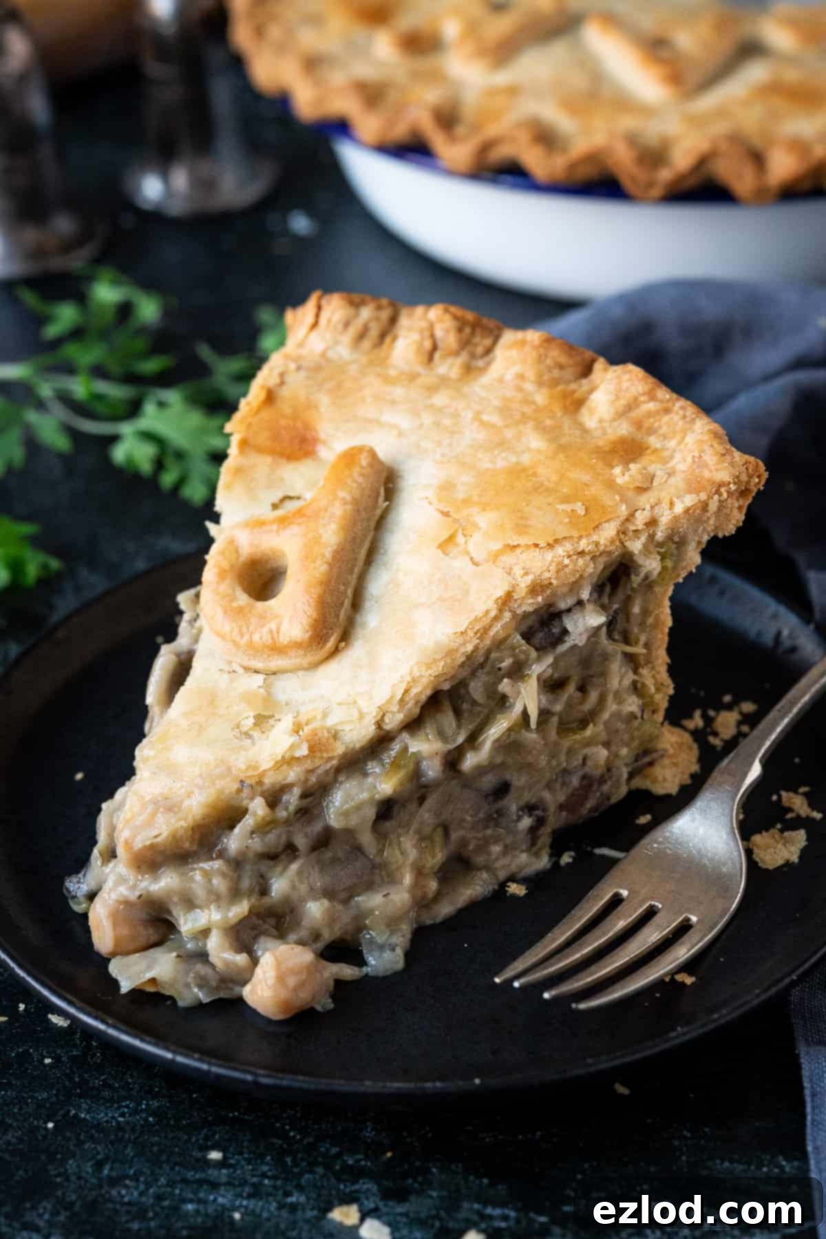 A slice of chickpea, leek and mushroom pie on a black plate.