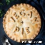 Chickpea, leek and mushroom pie with the words "vegan pie" written on top, on a dark background with forks, parsley, salt and pepper shakers and a grey cloth.
