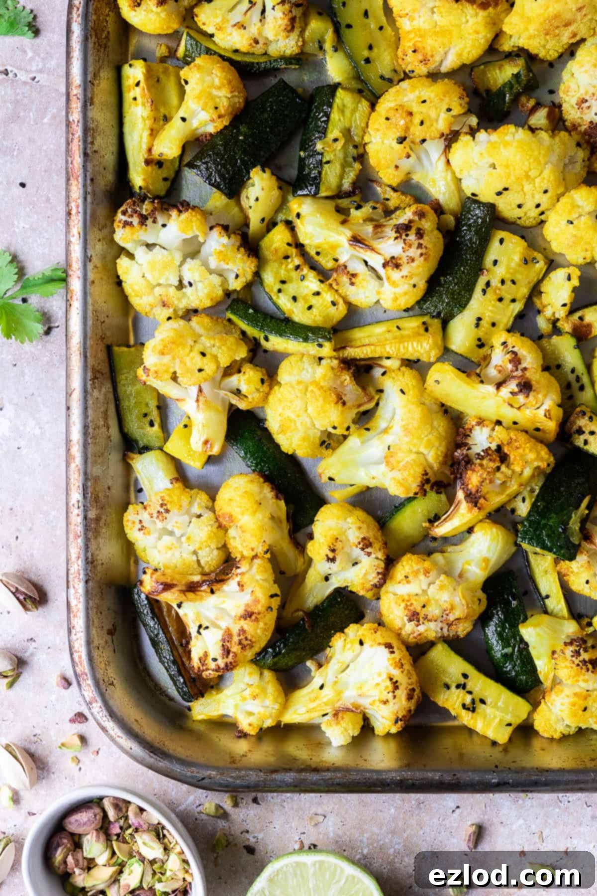 A close-up view of a metal roasting tray filled with spiced cauliflower florets and courgette strips, perfectly roasted to a golden brown, ready to be served.