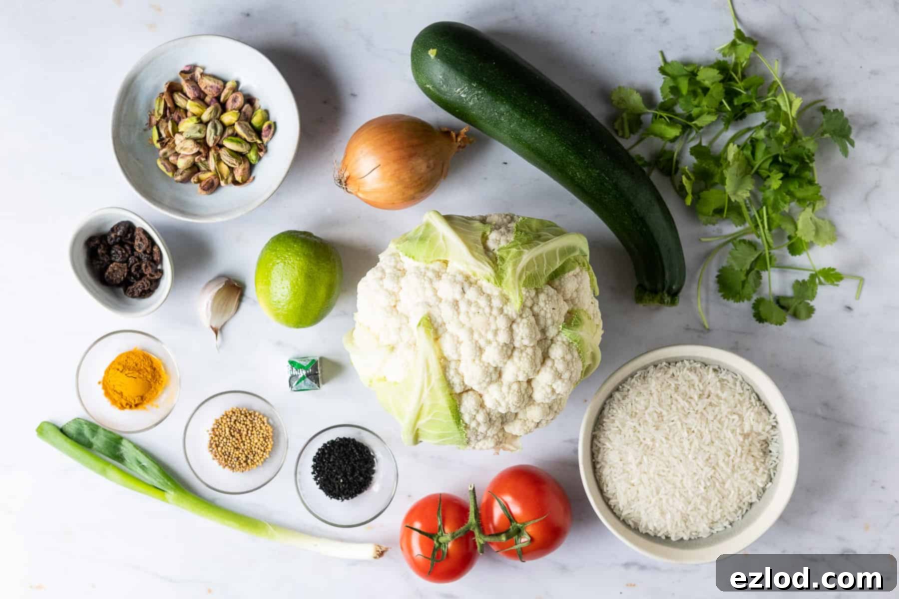 A neatly arranged flat lay of all the fresh ingredients required for making spiced cauliflower and courgette with yellow rice, including vegetables, spices, rice, and salsa components.