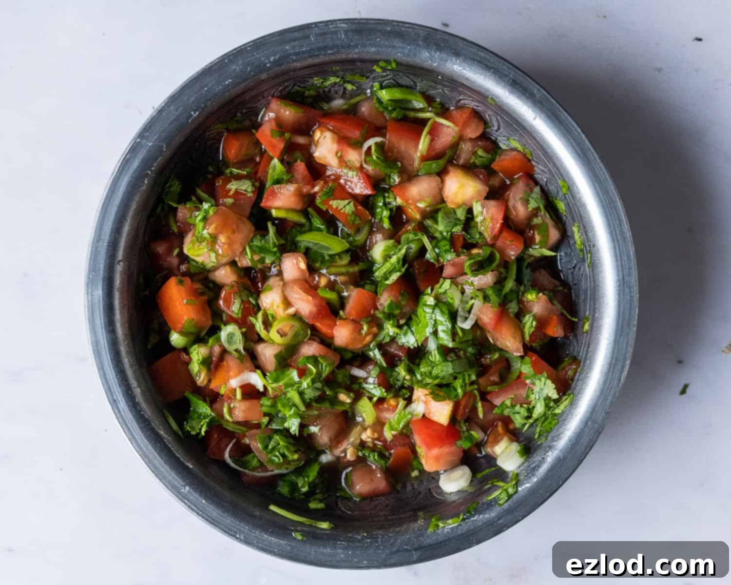 A close-up shot of a small bowl filled with vibrant, freshly made tomato lime salsa, featuring finely chopped tomatoes, green coriander, and hints of lime zest.