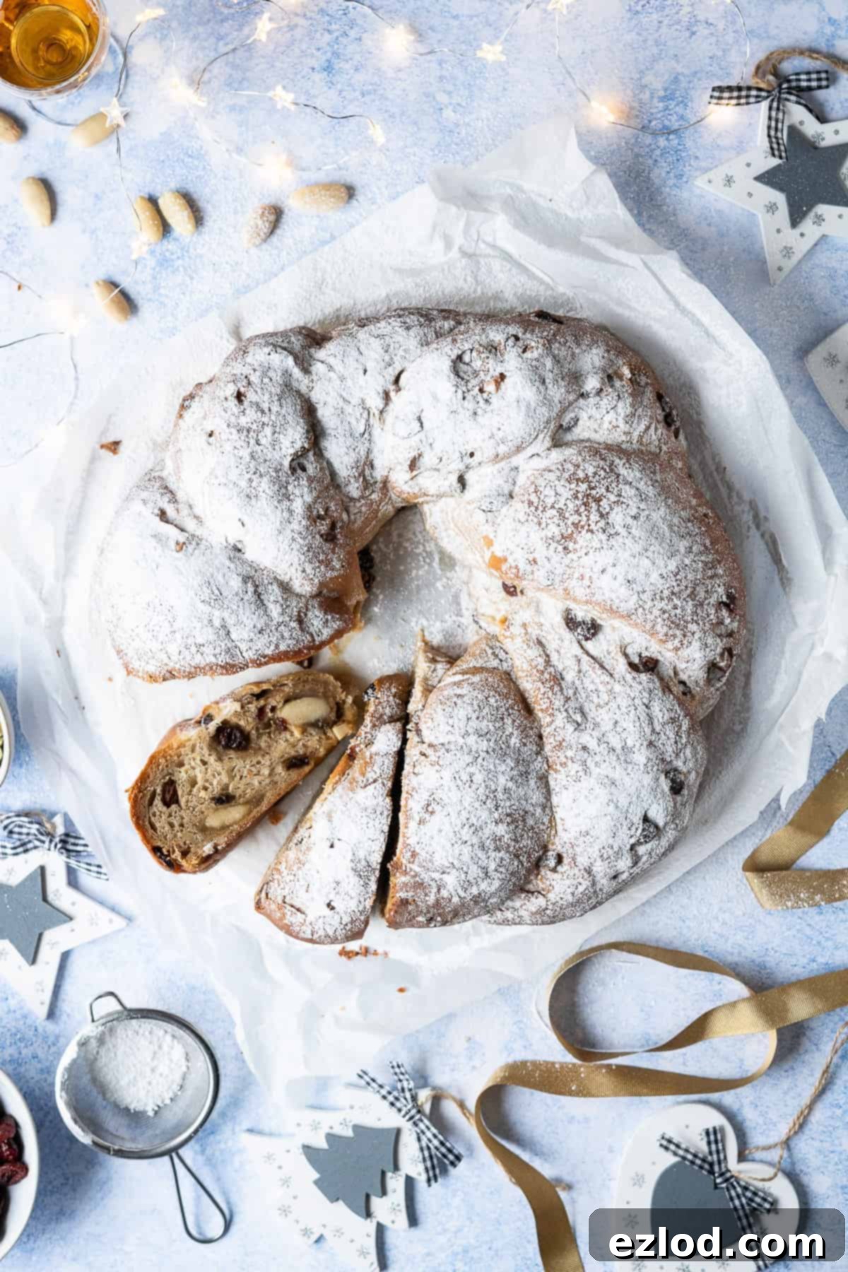 Vegan stollen wreath on a sheet of white baking parchment on a blue surface with christmas decorations and lights.