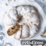 Vegan stollen wreath on a sheet of white baking parchment on a blue surface with christmas decorations and lights.
