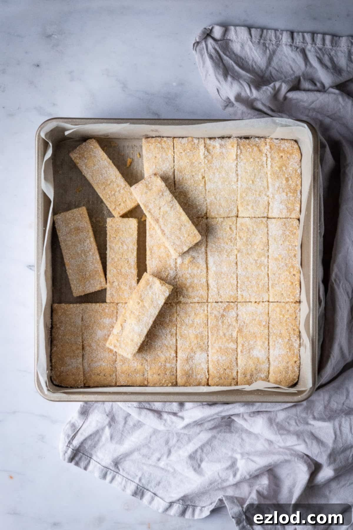 Vegan shortbread fingers perfectly arranged in a square metal cake tin, set against a elegant marble background with a soft grey cloth.