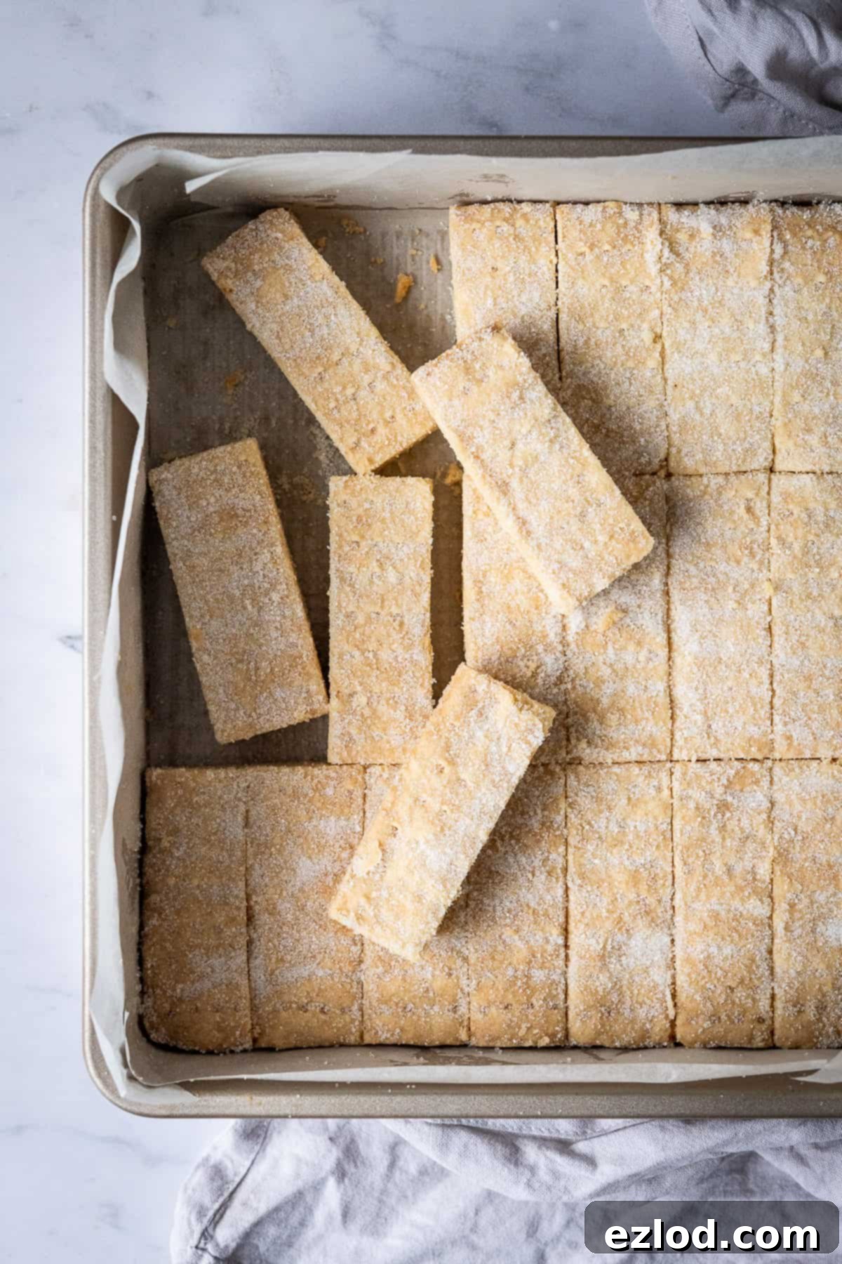 A close-up view of golden vegan shortbread fingers neatly arranged in a square metal cake tin, highlighting their delicious texture.