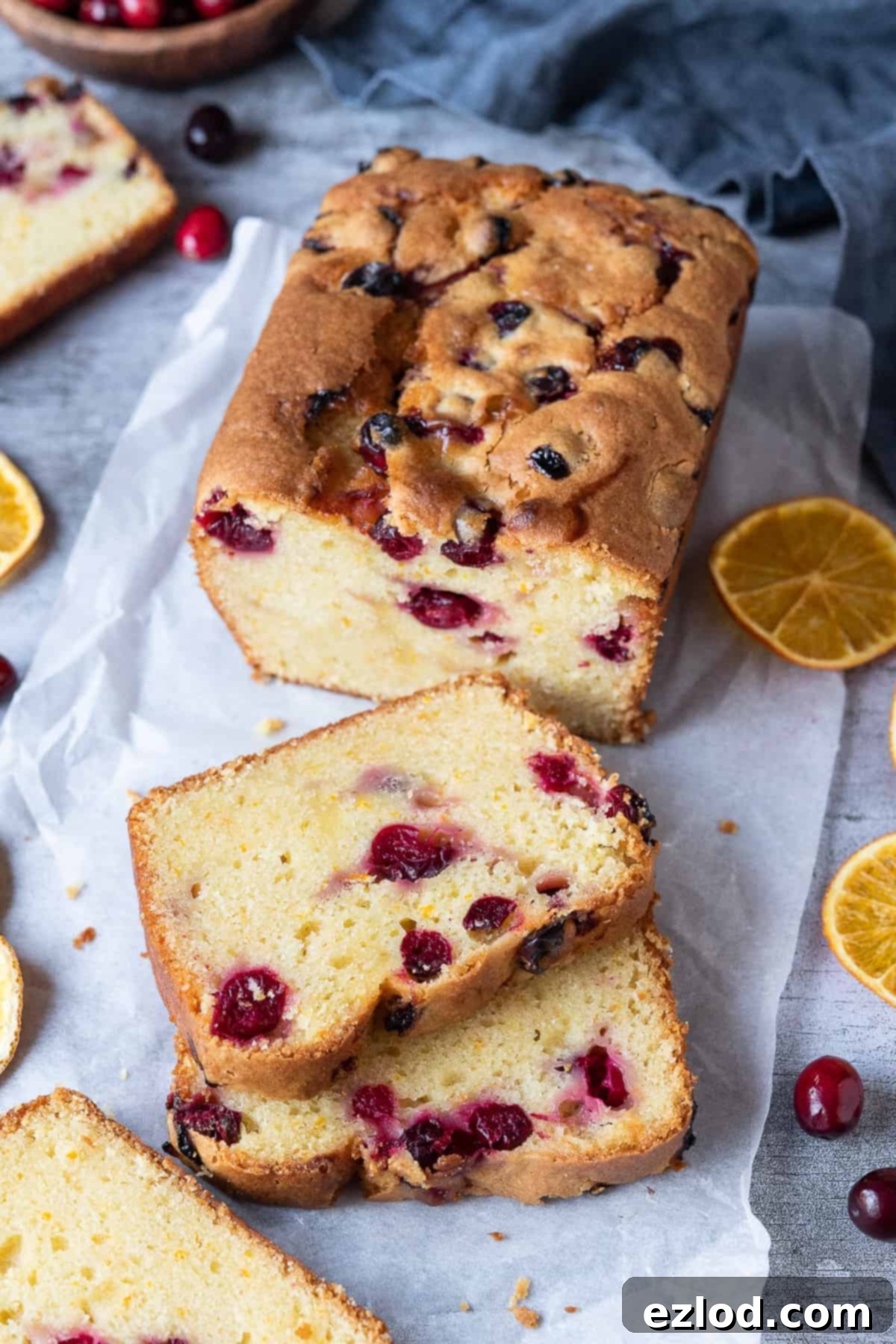 Vegan orange cranberry cake on a sheet of white baking parchment with dried orange slices and fresh cranberries.
