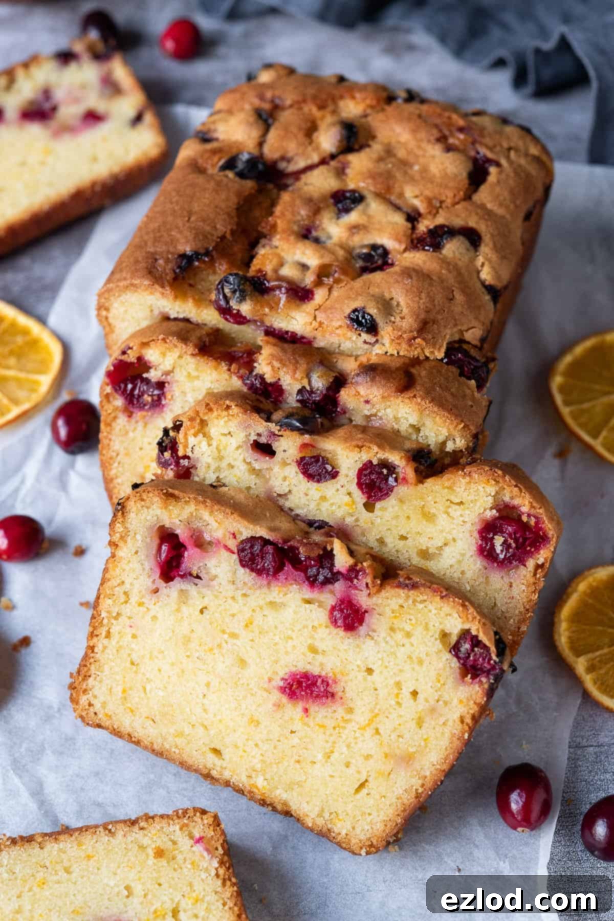 Sliced cranberry orange bread on a sheet of baking parchment on a grey background.