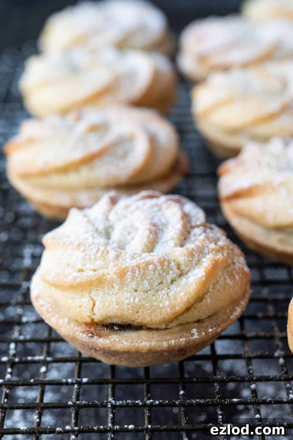 Close-up photo of a single vegan Viennese whirl mince pie on a metal cooling rack, highlighting its detailed piped topping and golden crust.
