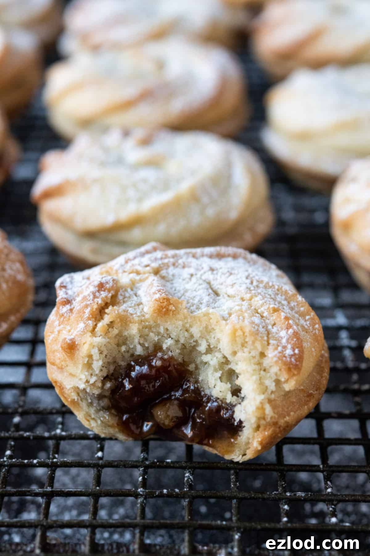 Close-up of a vegan Viennese whirl mince pie with a bite taken out, revealing the mincemeat filling and the delicate topping texture.