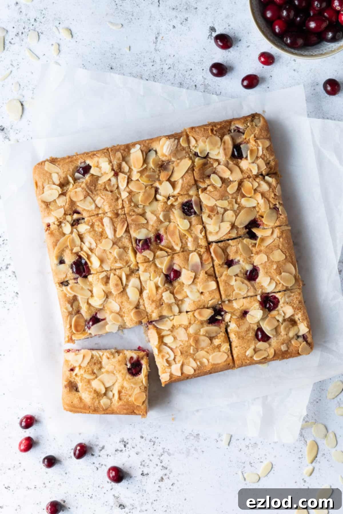 Vegan cranberry almond cake on a sheet of white baking parchment on a white surface with fresh cranberries.