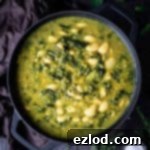 Spinach, lentil and butter bean soup in a black pan on a wooden table with fresh herbs, slices of bread and a bowl of salt.